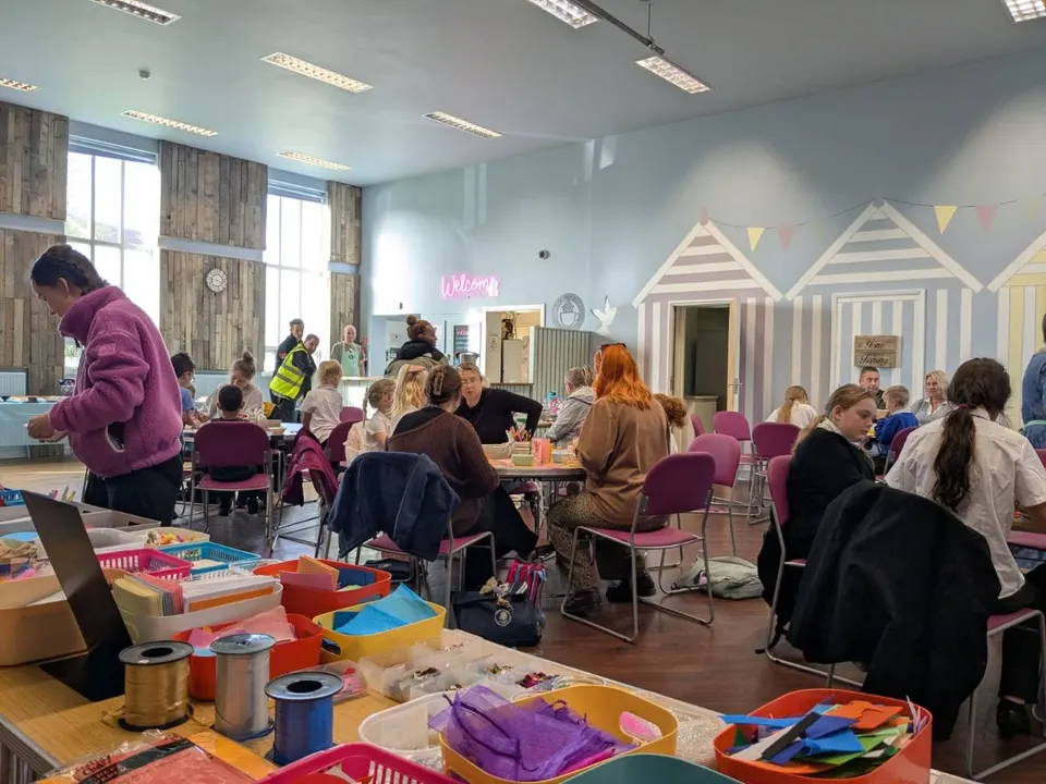 People gathered around tables for Tuesday afternoon crafts at Ark Café, with colourful craft materials in the foreground.