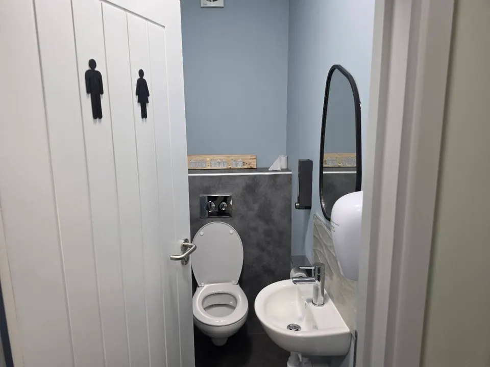 A completed toilet cubicle with pale blue walls, a washbasin and a dark-framed mirror.